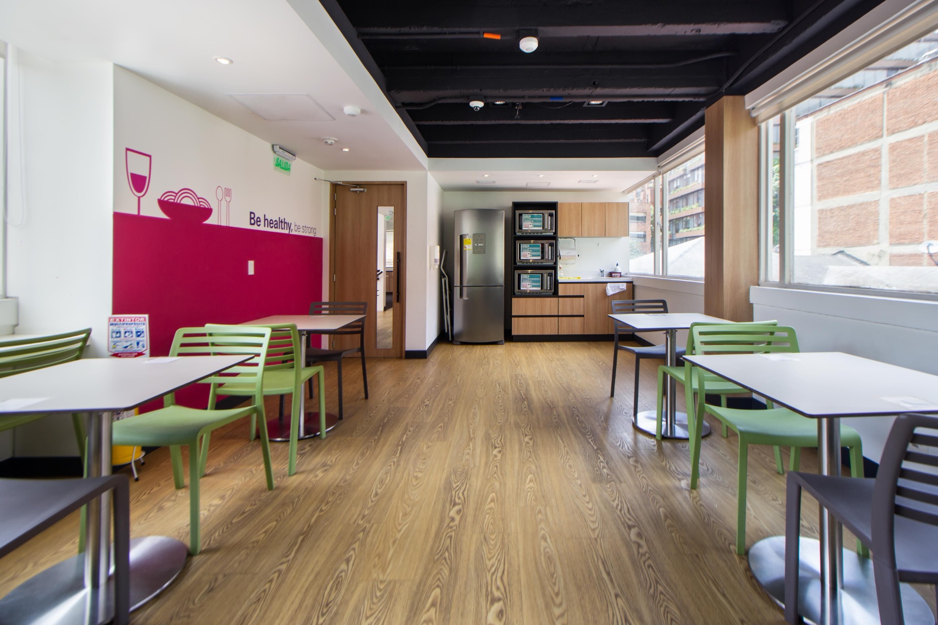 Bright cafeteria interior with colorful chairs, tables, vending machines, and a “Be healthy” wall mural.