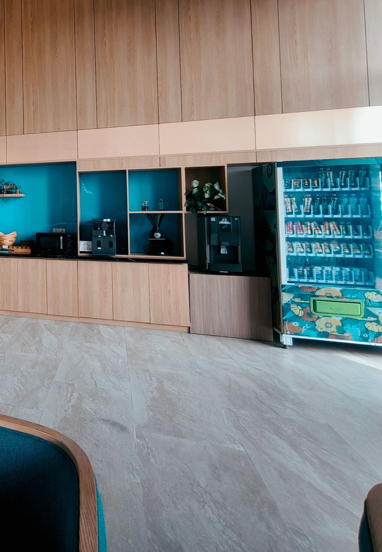 Modern break room with wooden cabinetry, built-in machines, and a brightly lit beverage vending refrigerator display.